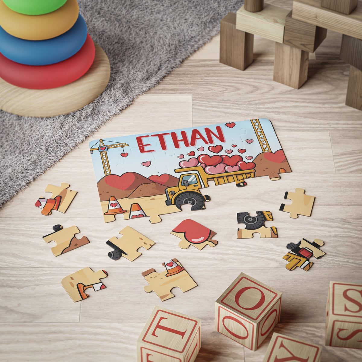 Personalized construction truck Valentine’s Day jigsaw puzzle displayed on a playroom floor with scattered jigsaw pieces. The puzzle features a dump truck carrying hearts and a customizable name printed across the top.