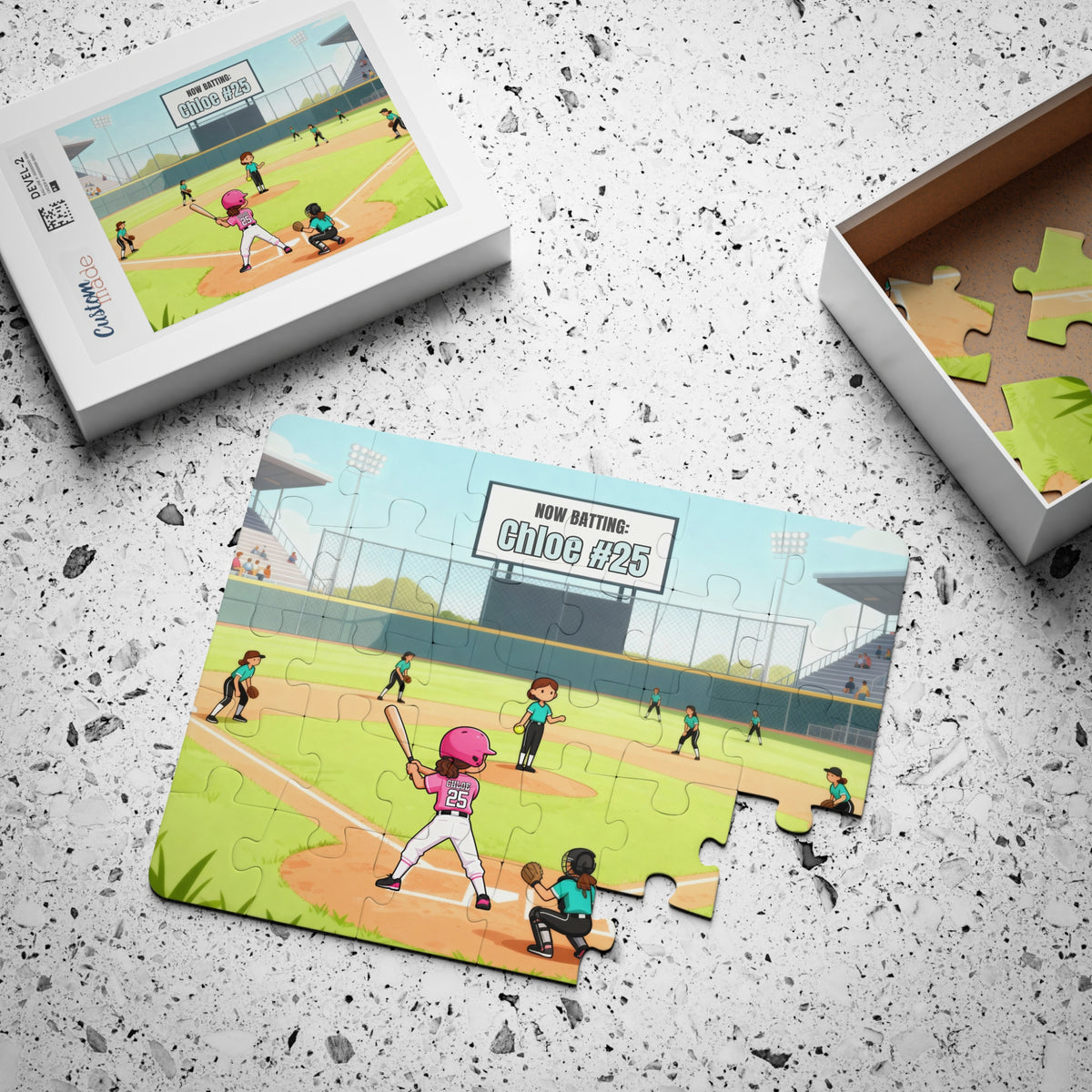 Jigsaw puzzle pieces spread across a surface next to packaging displaying a softball field design with a customizable player name and number shown on the jersey and scoreboard.
