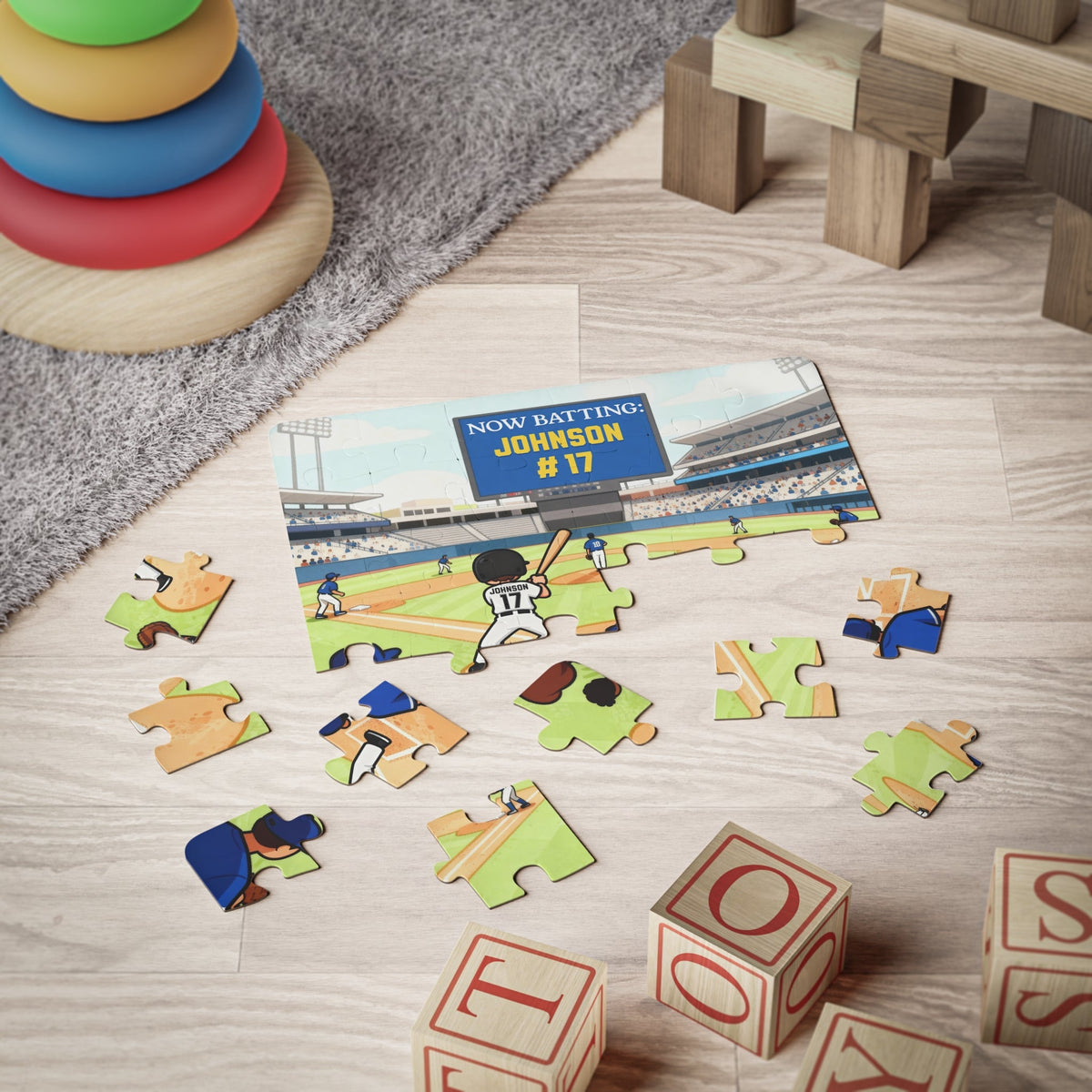 Personalized baseball-themed kids puzzle partially assembled on a playroom floor, featuring a cartoon baseball player at bat in a stadium. The custom name “Johnson” and number “17” appear on the scoreboard and jersey, showing how the puzzle looks during play.