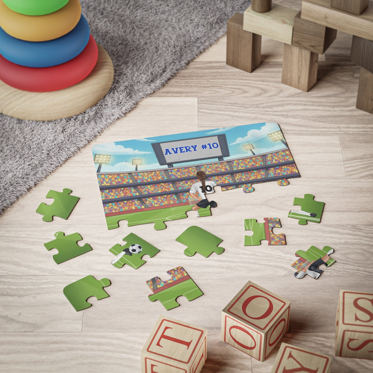 Custom 30-piece girls soccer name puzzle shown partially assembled on a playroom floor, featuring a young soccer player with a personalized name and number on the jersey, surrounded by loose puzzle pieces to show scale and size.