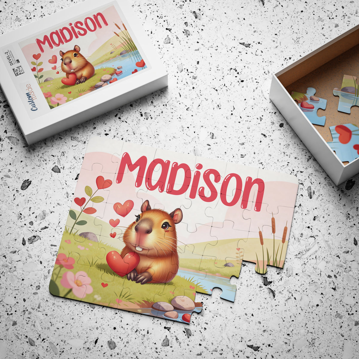 Personalized capybara jigsaw puzzle with a customizable name printed across the top, shown completed alongside its matching puzzle box and an open box displaying loose jigsaw pieces.