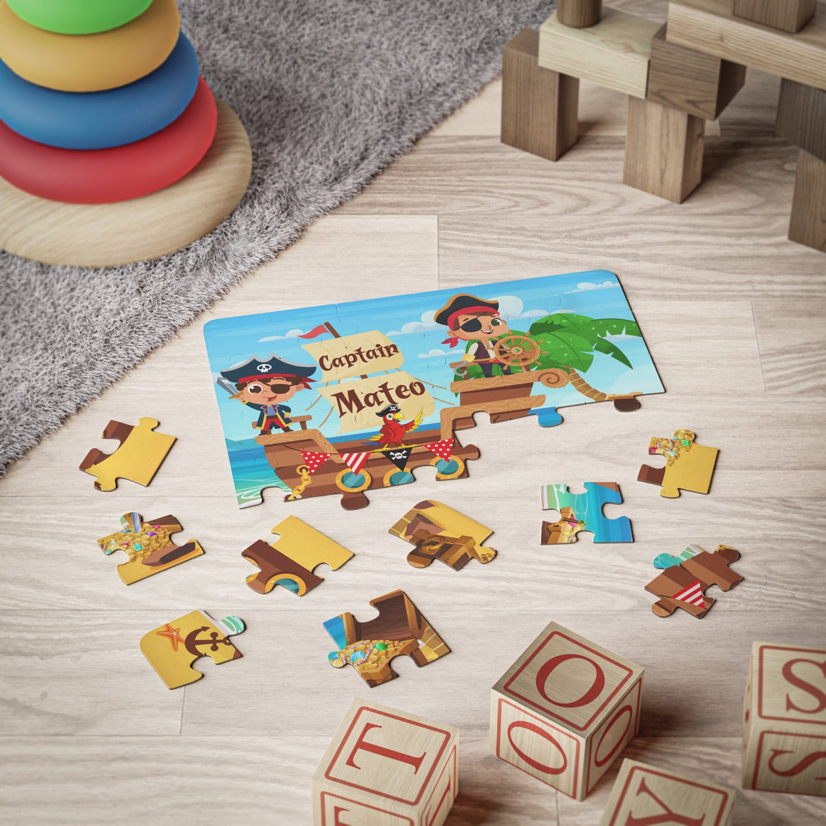 Personalized kids jigsaw puzzle featuring a pirate ship scene with cartoon pirates and ocean background. The child’s chosen name is printed prominently on the puzzle design. Image shows the assembled puzzle with loose jigsaw pieces arranged on the floor to show scale and piece style.