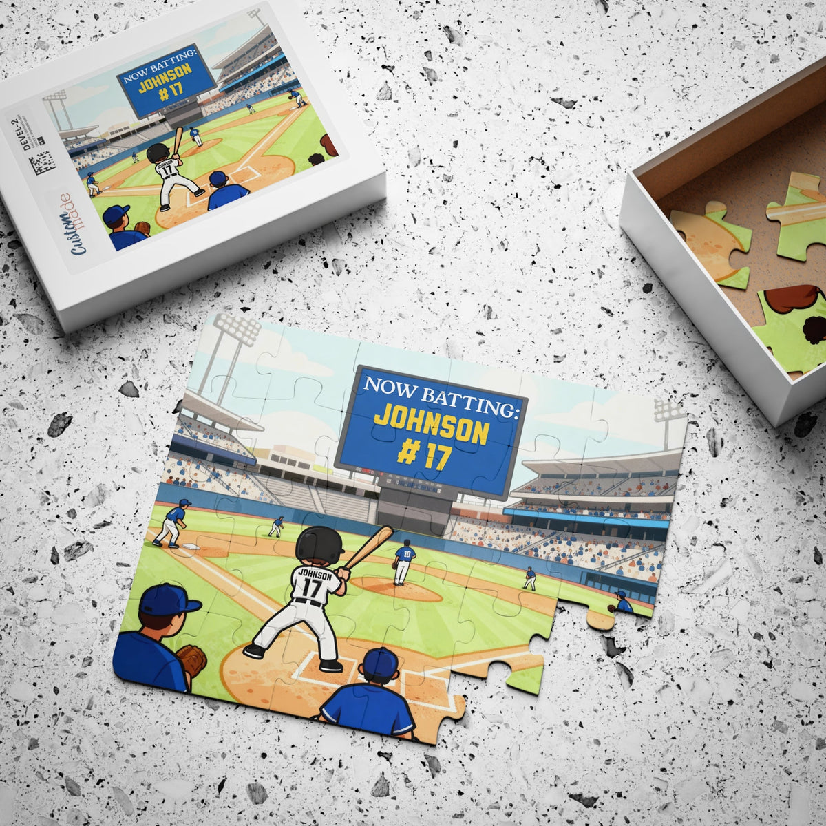Custom baseball name puzzle displayed next to its gift box, showing a stadium scene with a young player at home plate. The puzzle features a personalized scoreboard and jersey number, demonstrating how the finished puzzle looks as a keepsake gift.