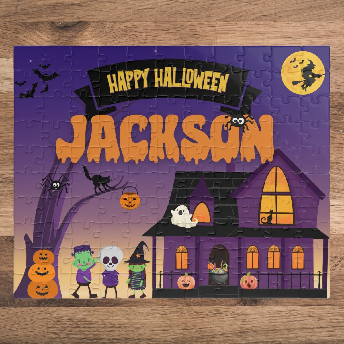 Personalized 110-piece Halloween jigsaw puzzle for kids featuring a spooky haunted house scene with trick-or-treaters, bats, pumpkins, and moon. Puzzle includes a customizable name printed prominently across the top of the design.