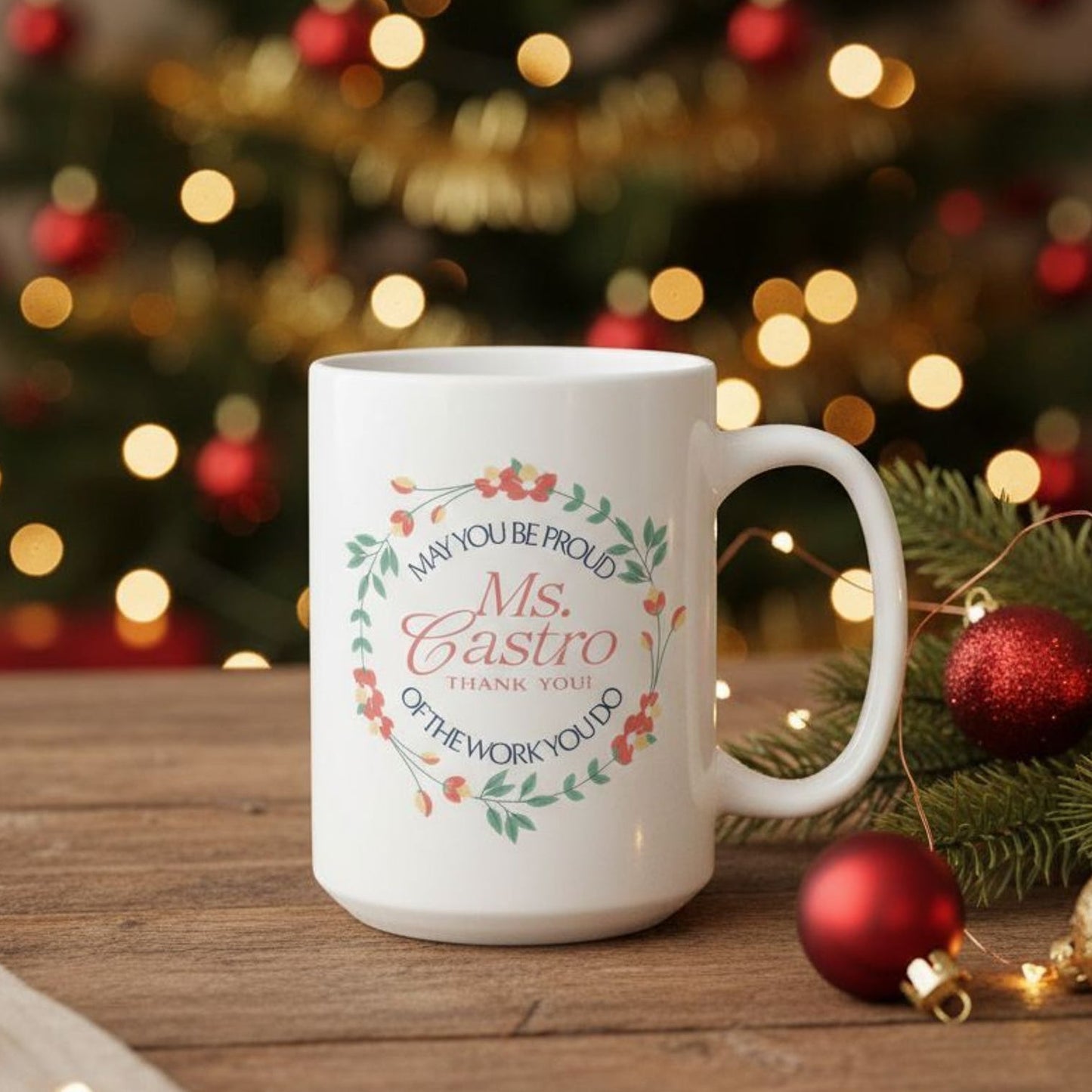 Personalized floral ceramic mug displayed in a holiday setting, showing the same wreath design with a customizable name printed in the center on the front of the mug and the quote “May You Be Proud of the Work You Do.”