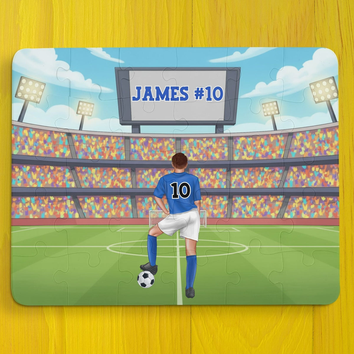 Personalized boys soccer jigsaw puzzle showing a player standing on a stadium field, with a customizable name displayed on the scoreboard and a customizable number on the back of the jersey.