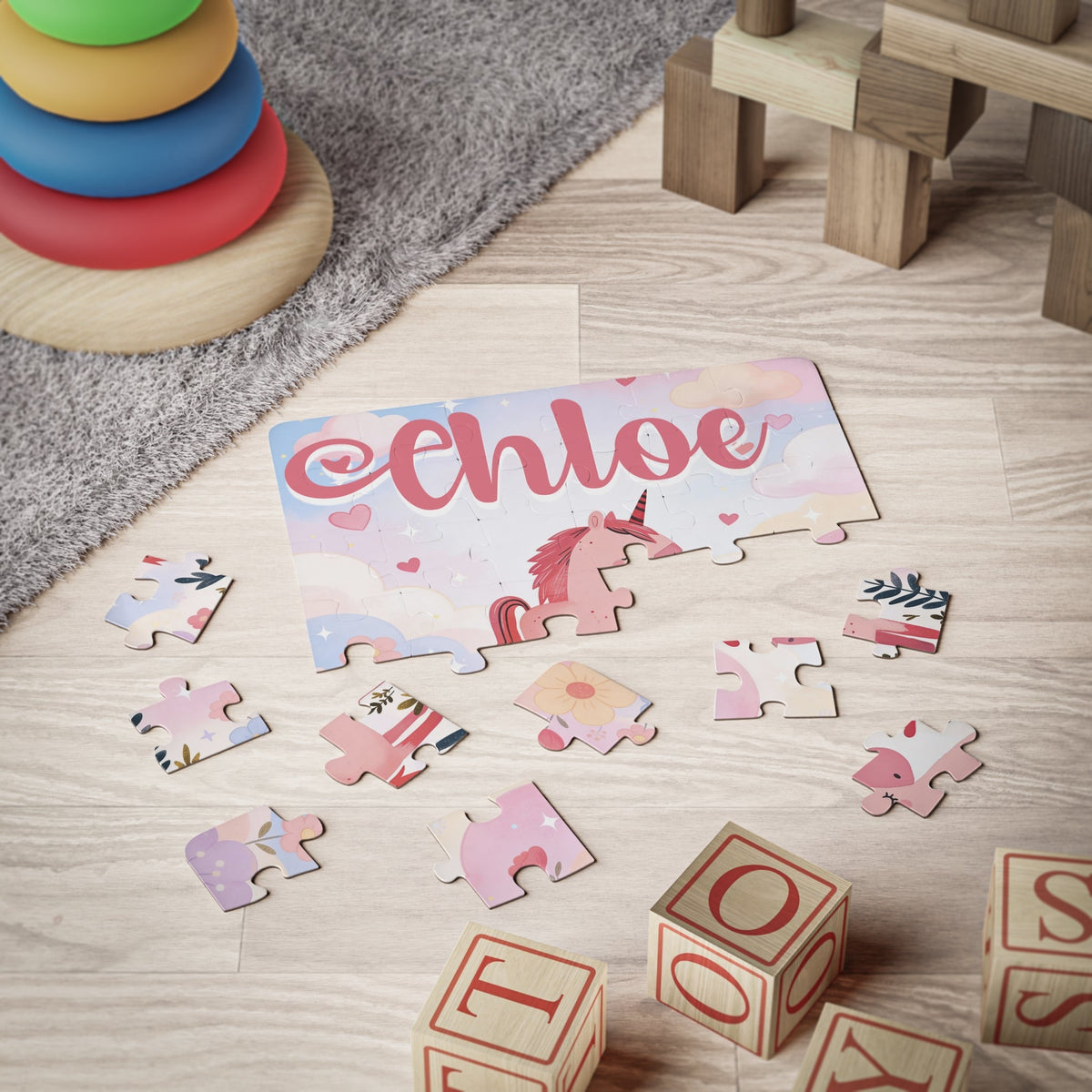 Personalized kids jigsaw puzzle shown partially assembled on the floor with scattered jigsaw pieces, featuring a unicorn illustration and a customizable child’s name printed across the top of the puzzle.