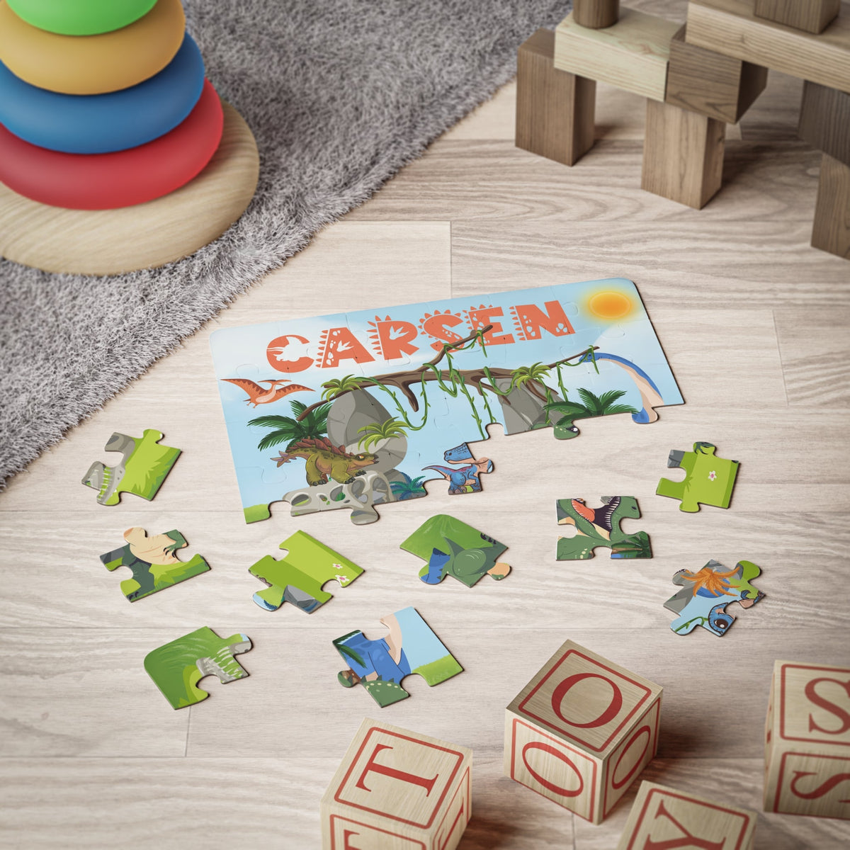 Personalized dinosaur jigsaw puzzle for kids with a customizable name displayed across the top of the puzzle. A colorful jungle dinosaur scene with scattered jigsaw pieces shown during play. Name is customized by the customer and appears prominently on the puzzle design.