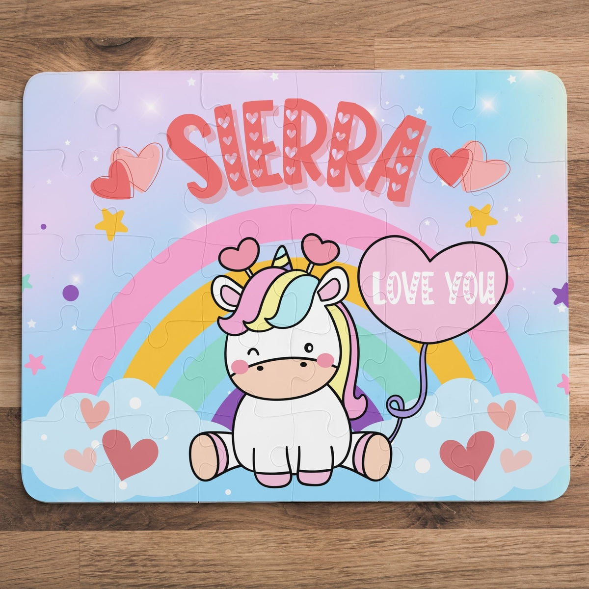 Personalized unicorn name puzzle for kids featuring a cute cartoon unicorn sitting on clouds with a rainbow, hearts, and a heart-shaped balloon that says “Love You.” The child’s name is customizable and appears large across the top of the puzzle (shown as “Sierra”), making this a custom 30-piece jigsaw designed for toddlers and young children.