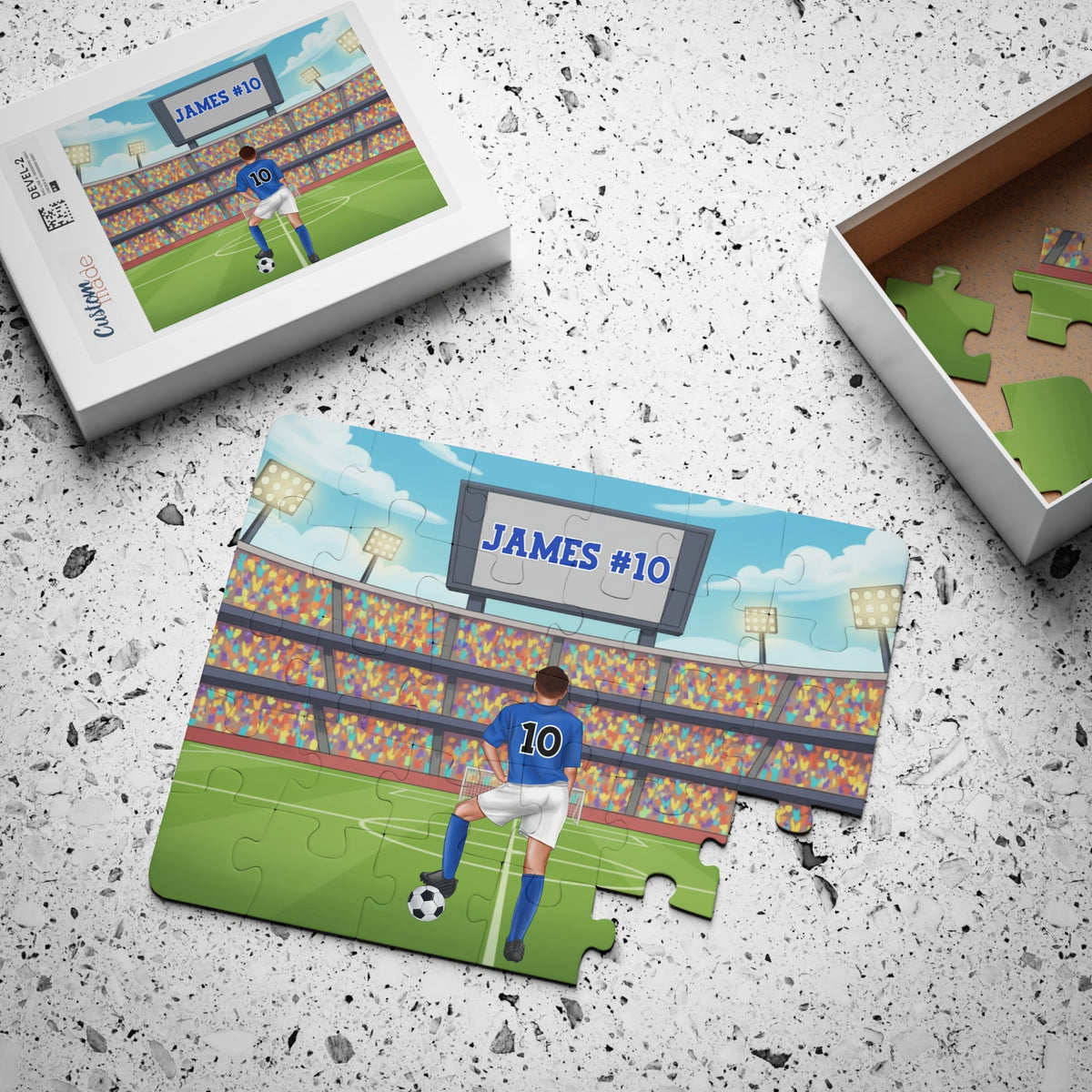 Completed personalized boys soccer jigsaw puzzle next to its box, featuring a stadium scene with a customizable name on the scoreboard and a customizable number on the back of the jersey.