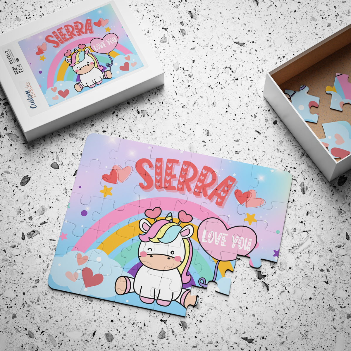 Personalized unicorn jigsaw puzzle with a customizable name displayed across the top of the design, shown assembled with a matching puzzle box. The name is customized by the customer and appears prominently on the puzzle front.
