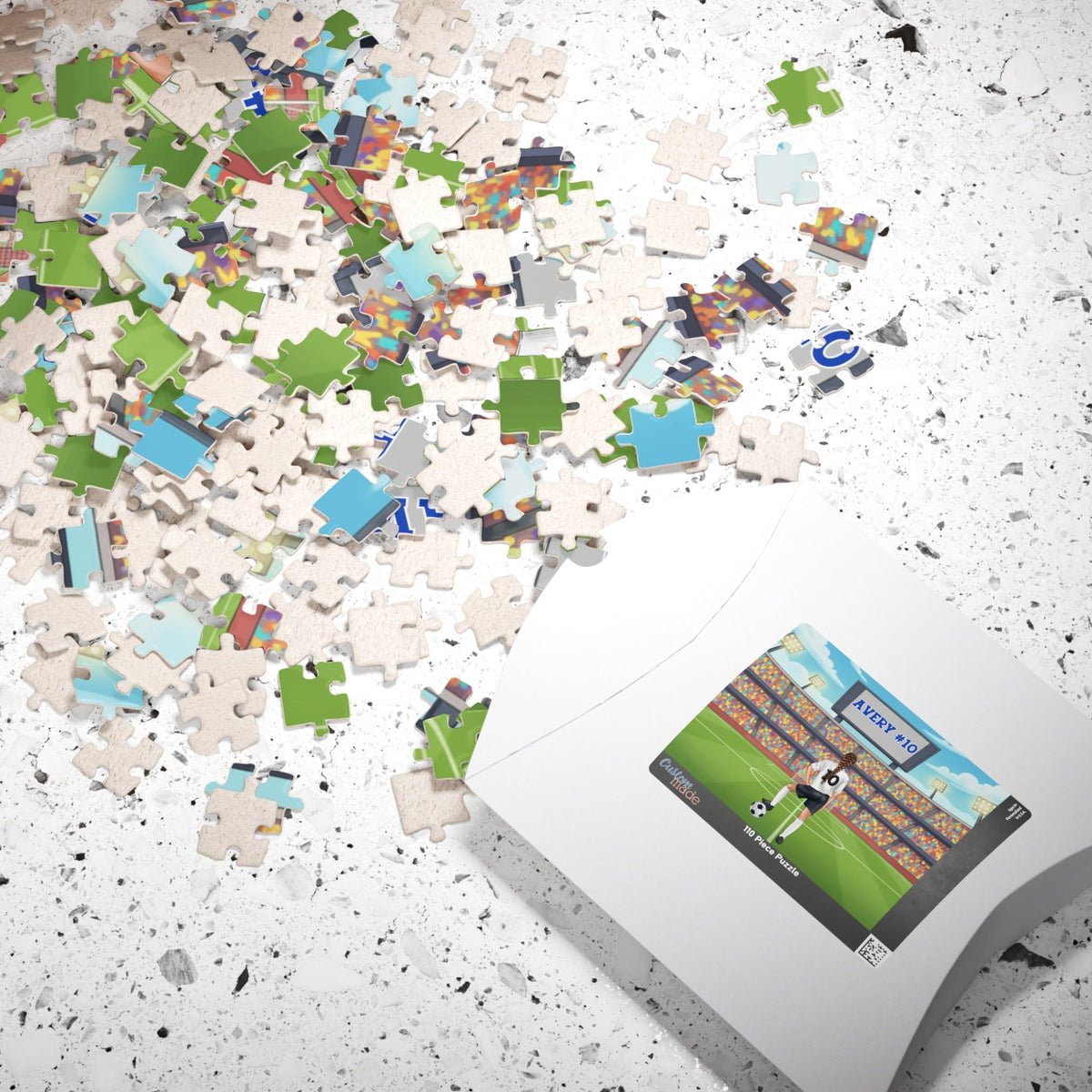 Lifestyle photo of a personalized girls soccer jigsaw puzzle with scattered jigsaw pieces on a tabletop next to the puzzle box, showing a stadium scene with a customizable name on the scoreboard and a customizable number on the player’s jersey.