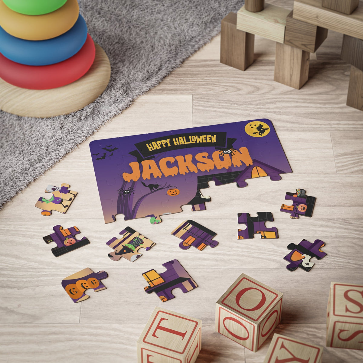 Personalized Halloween name puzzle shown on a playroom floor with scattered jigsaw pieces. The 30-piece kids puzzle features a spooky house and trick-or-treat characters, with a customizable name printed prominently at the top of the puzzle.