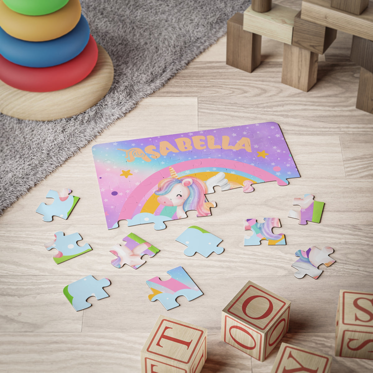 Personalized 30-piece kids jigsaw puzzle shown in a playroom setting with large jigsaw pieces scattered around, featuring a unicorn and rainbow design with a customizable name across the puzzle.