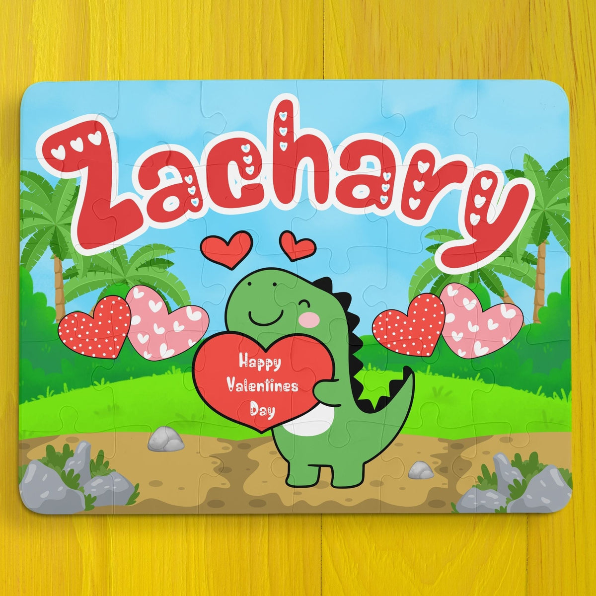 Personalized dinosaur name puzzle for kids featuring a cute green dino holding a heart that says “Happy Valentine’s Day,” surrounded by hearts and palm trees. The child’s name is customizable and appears large across the top of the puzzle (shown as “Zachary”), making this a custom 30-piece jigsaw designed for toddlers and young children.