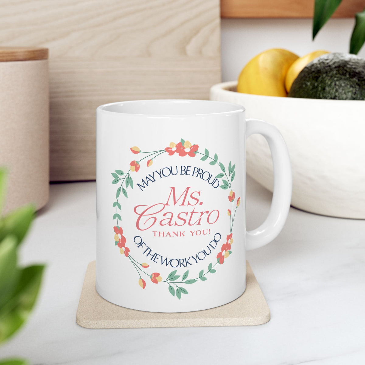 Personalized floral ceramic mug shown on a table, featuring a decorative wreath design with a customizable name centered on the front and the quote “May You Be Proud of the Work You Do.”