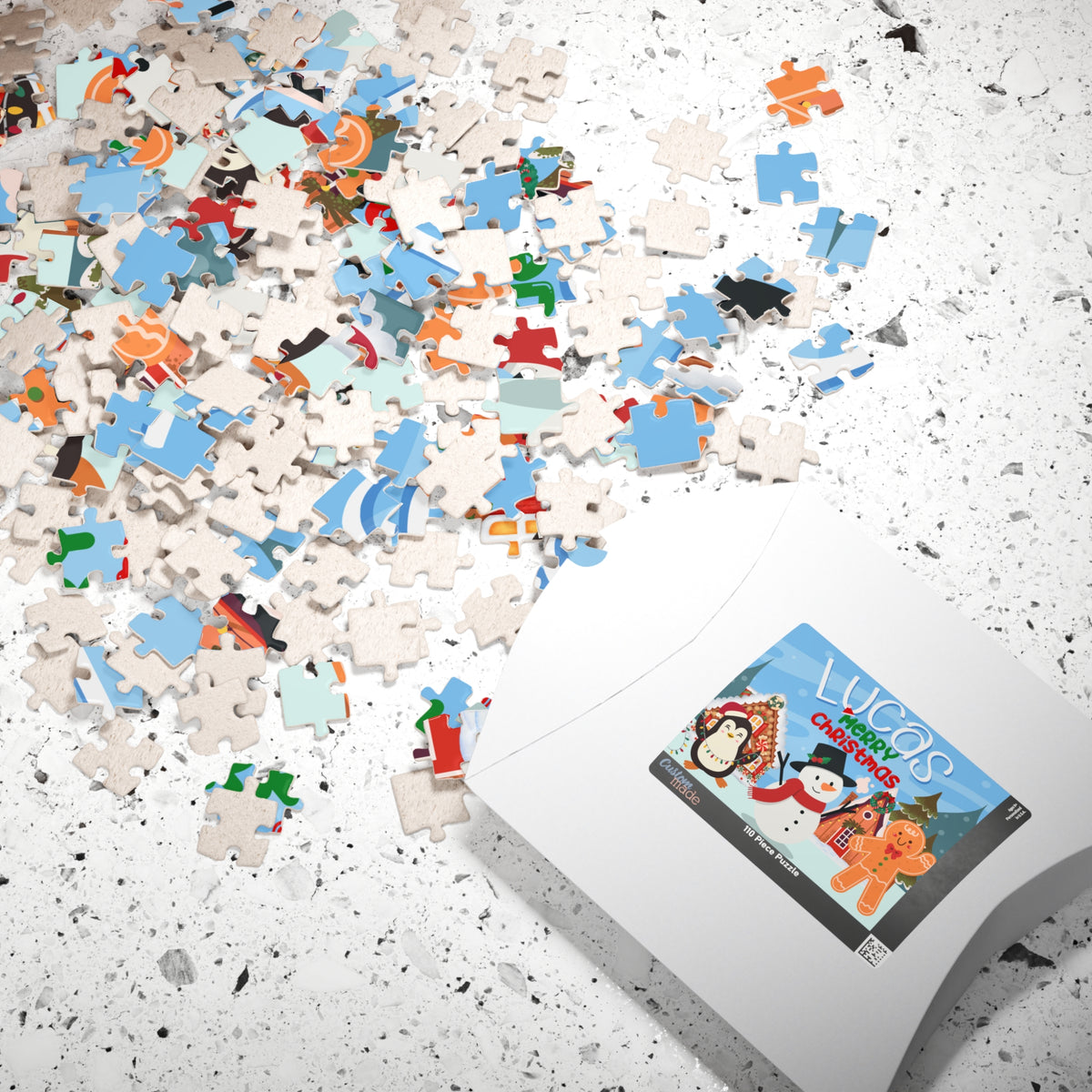 Personalized Christmas puzzle pieces scattered beside the puzzle box featuring a custom name with a snowman, penguin, gingerbread cookie, and festive holiday scene.