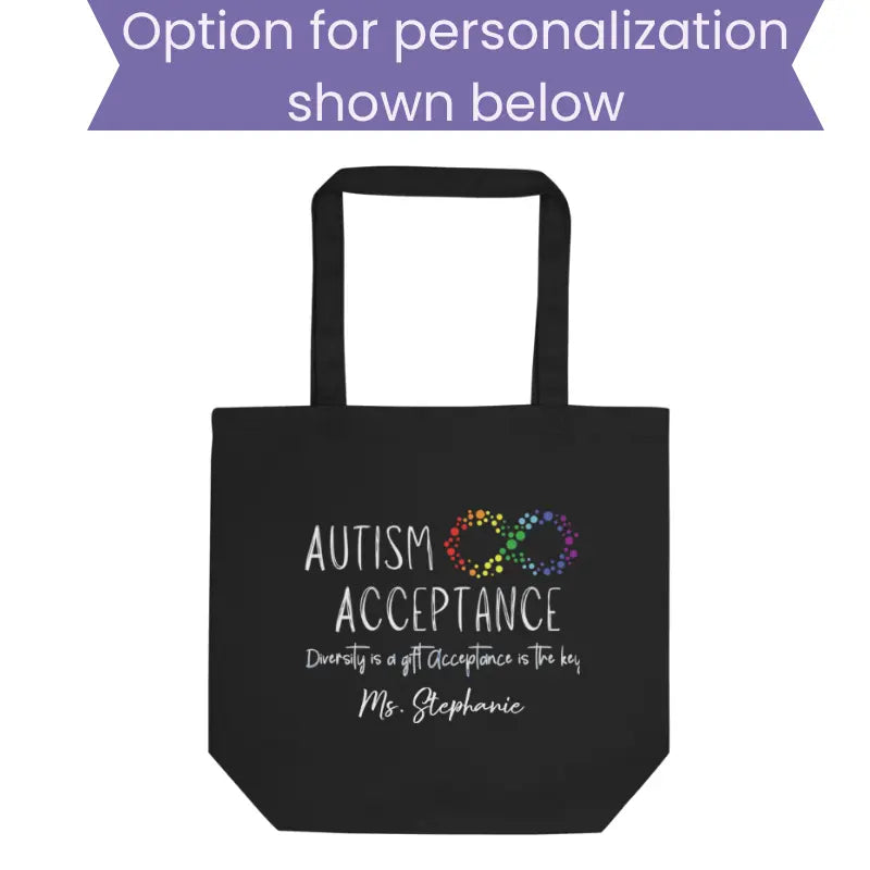 Option for personalization example black cotton canvas tote bag mockup showing an autism acceptance design with a customizable name printed below the main graphic on the front of the bag.