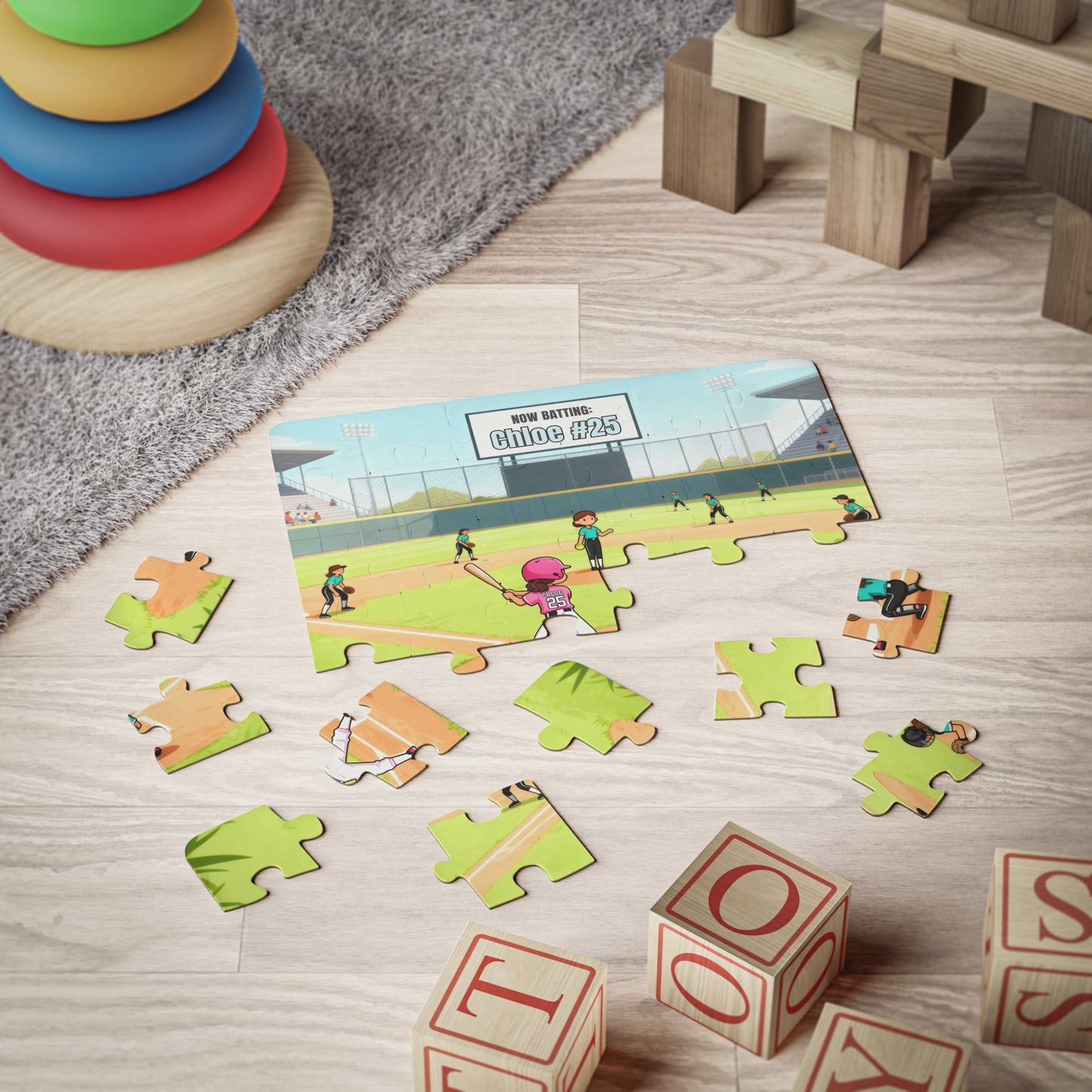 30-piece personalized softball puzzle partially assembled on a playroom floor with scattered pieces, showing a softball field scene with a customizable name and number on the jersey and scoreboard, surrounded by children’s toys.