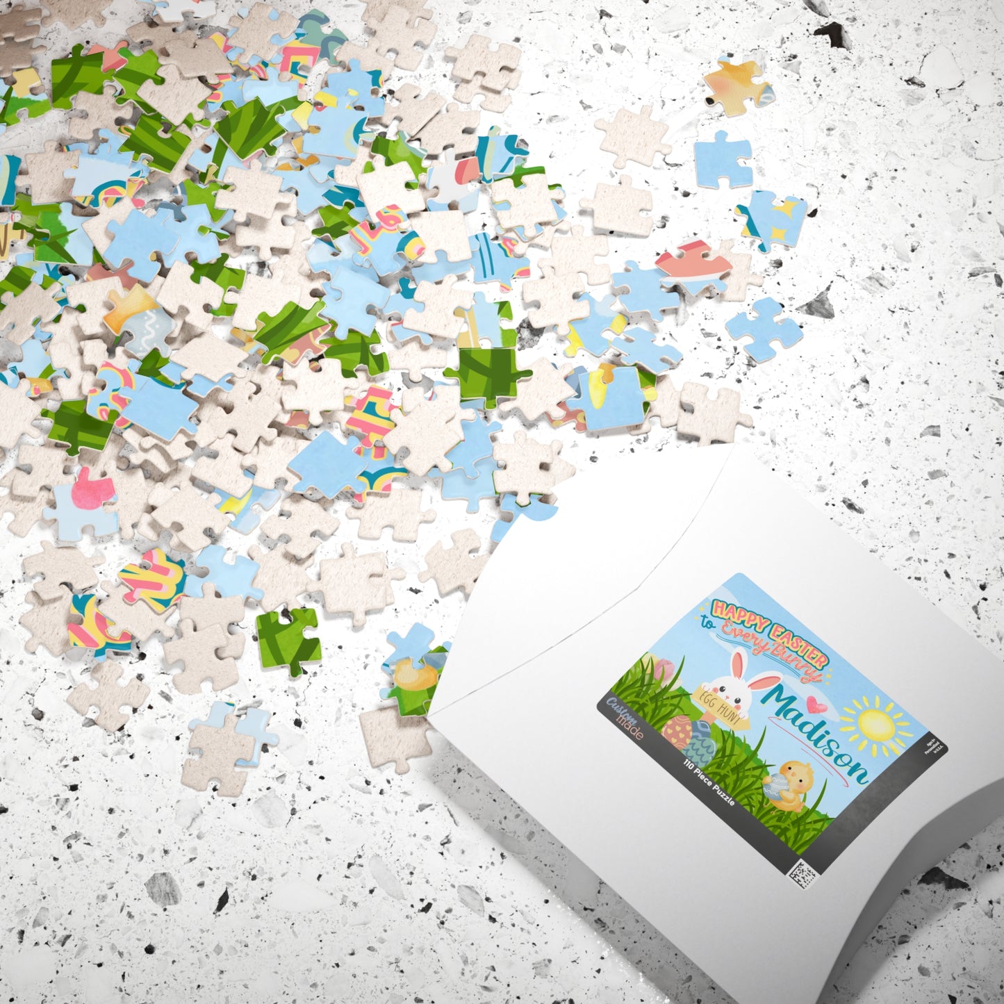 Personalized Easter-themed 110-piece jigsaw puzzle displayed with scattered jigsaw pieces and the puzzle box. Features a cheerful spring design with a bunny and a customizable name printed on the puzzle.