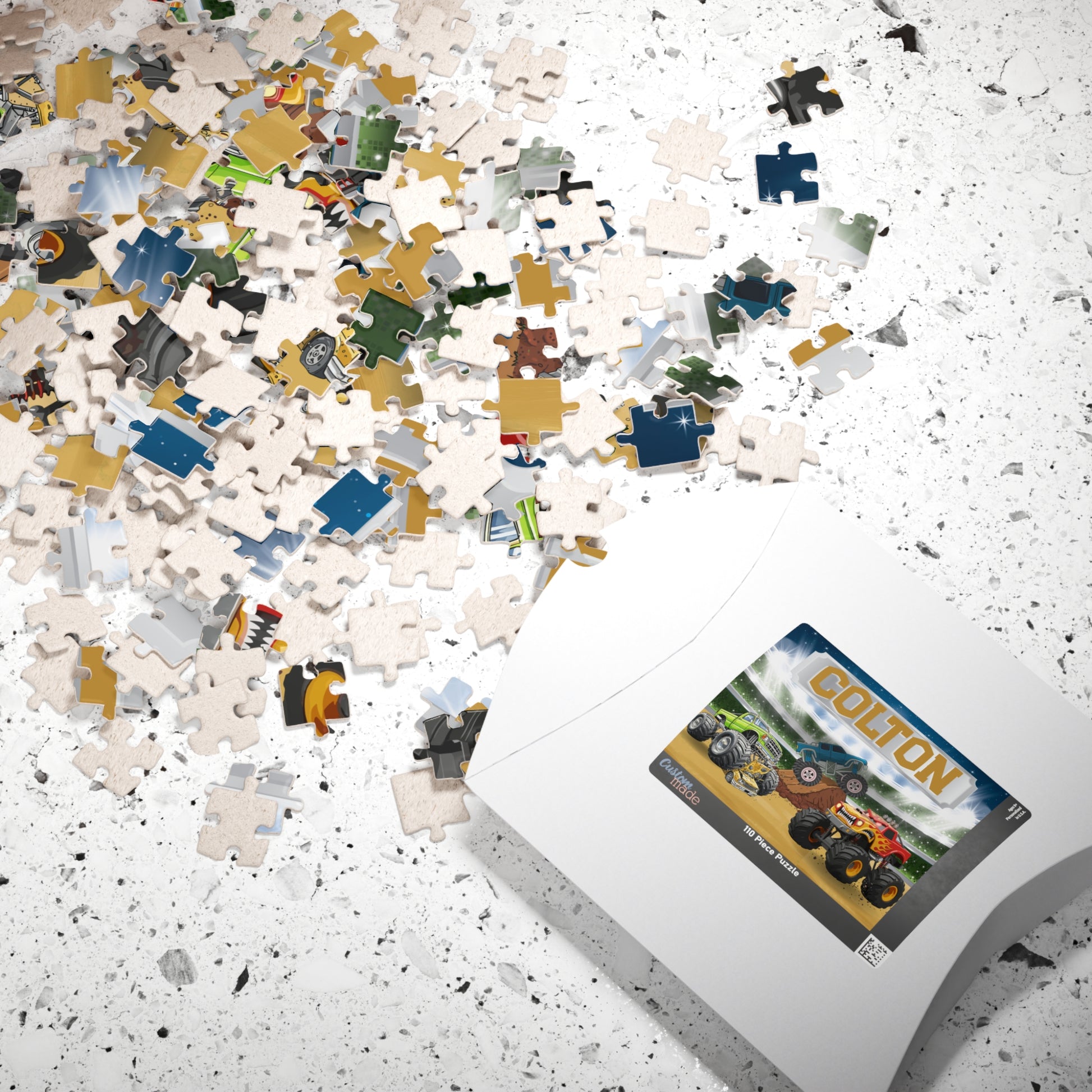 Scattered puzzle pieces next to packaging showing monster truck design with customizable name at the top, highlighting personalized jigsaw puzzle for kids who love trucks.