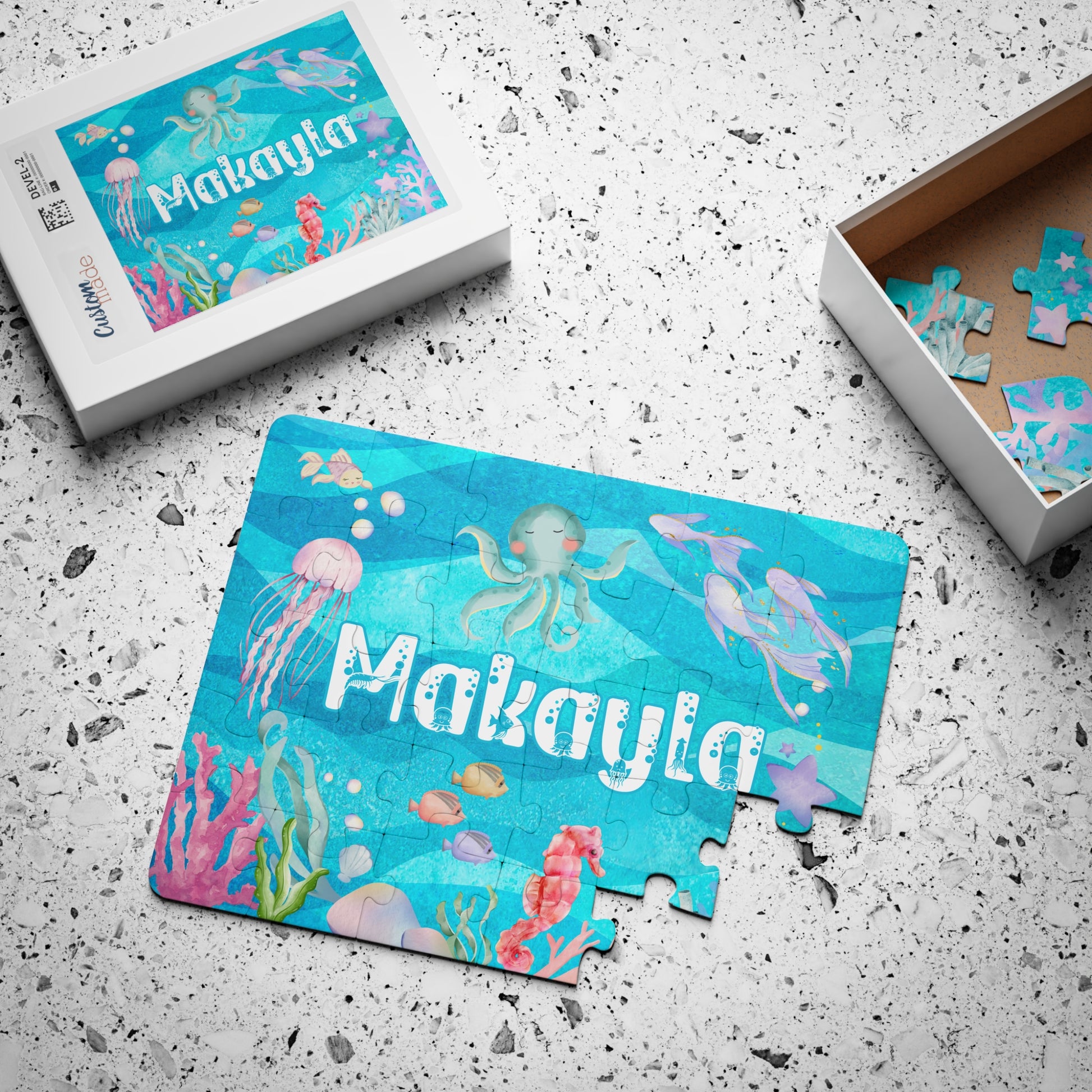 Custom under-the-sea name puzzle for kids displayed with matching gift box and loose pieces, showing octopus, jellyfish, coral, and fish illustrations.