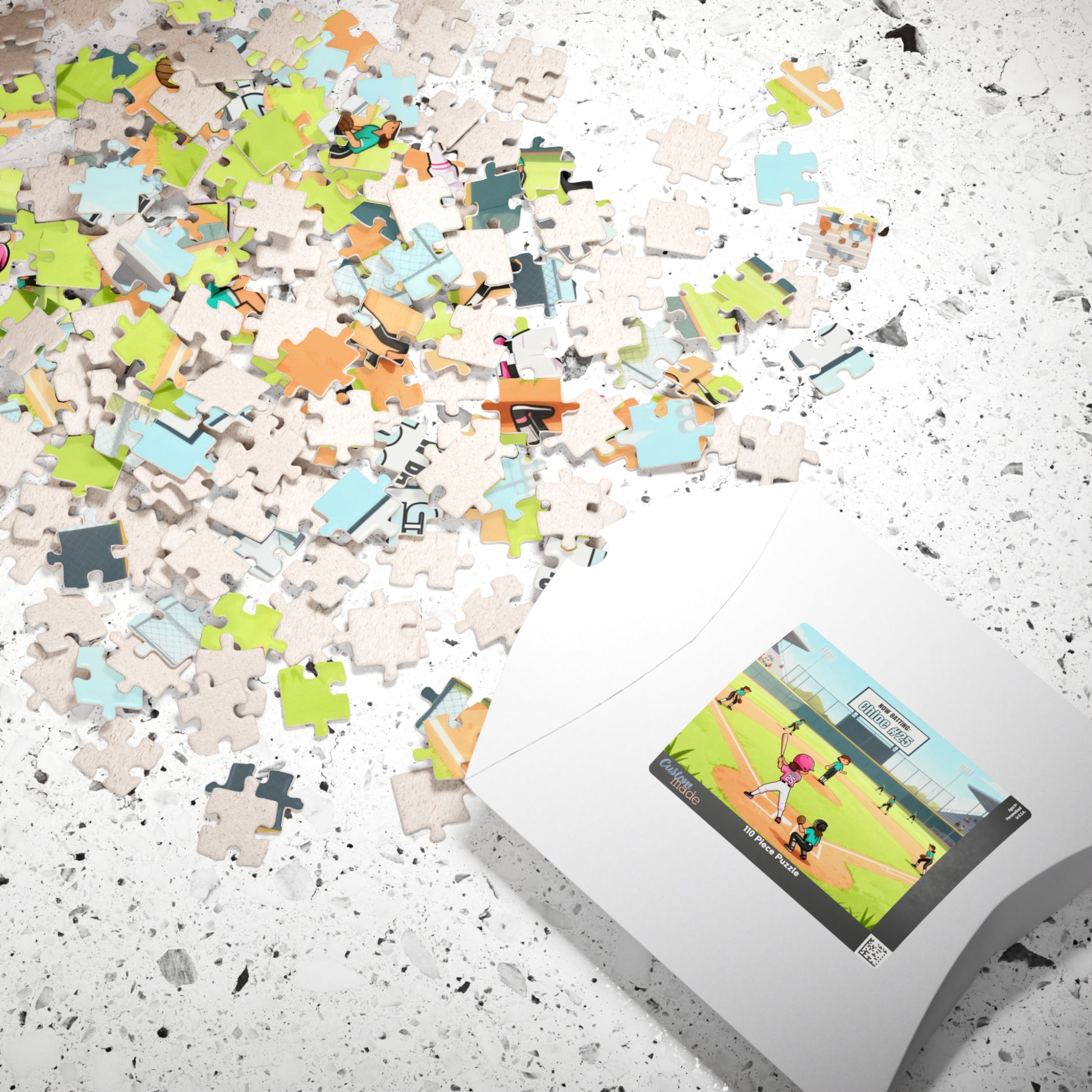 Jigsaw puzzle pieces scattered on a surface beside packaging displaying a softball field scene with a customizable player name and number shown on the jersey and scoreboard.