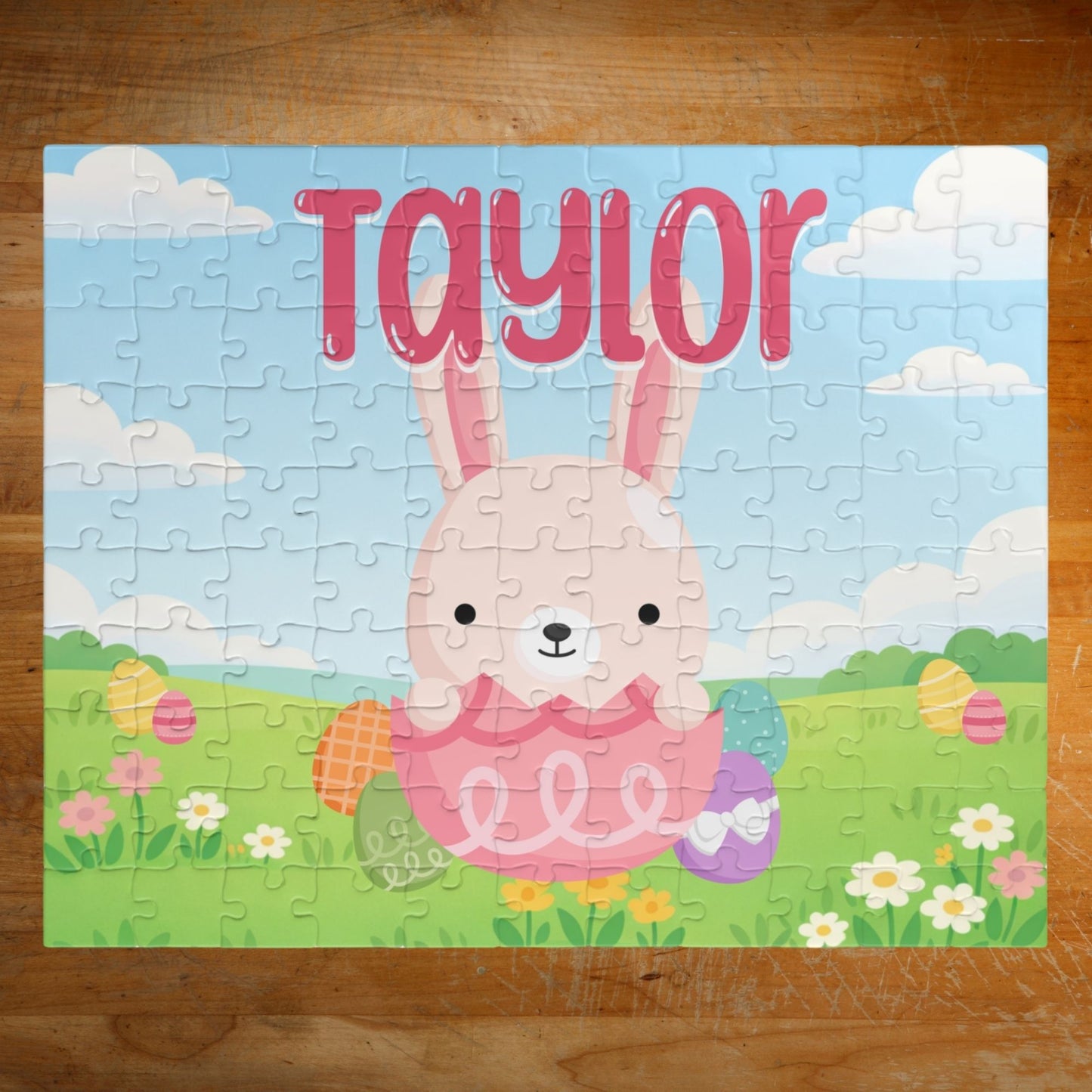 Fully assembled personalized Easter bunny jigsaw puzzle featuring a cheerful bunny sitting in a decorated egg within a spring meadow scene, with a customizable name printed across the top of the puzzle.