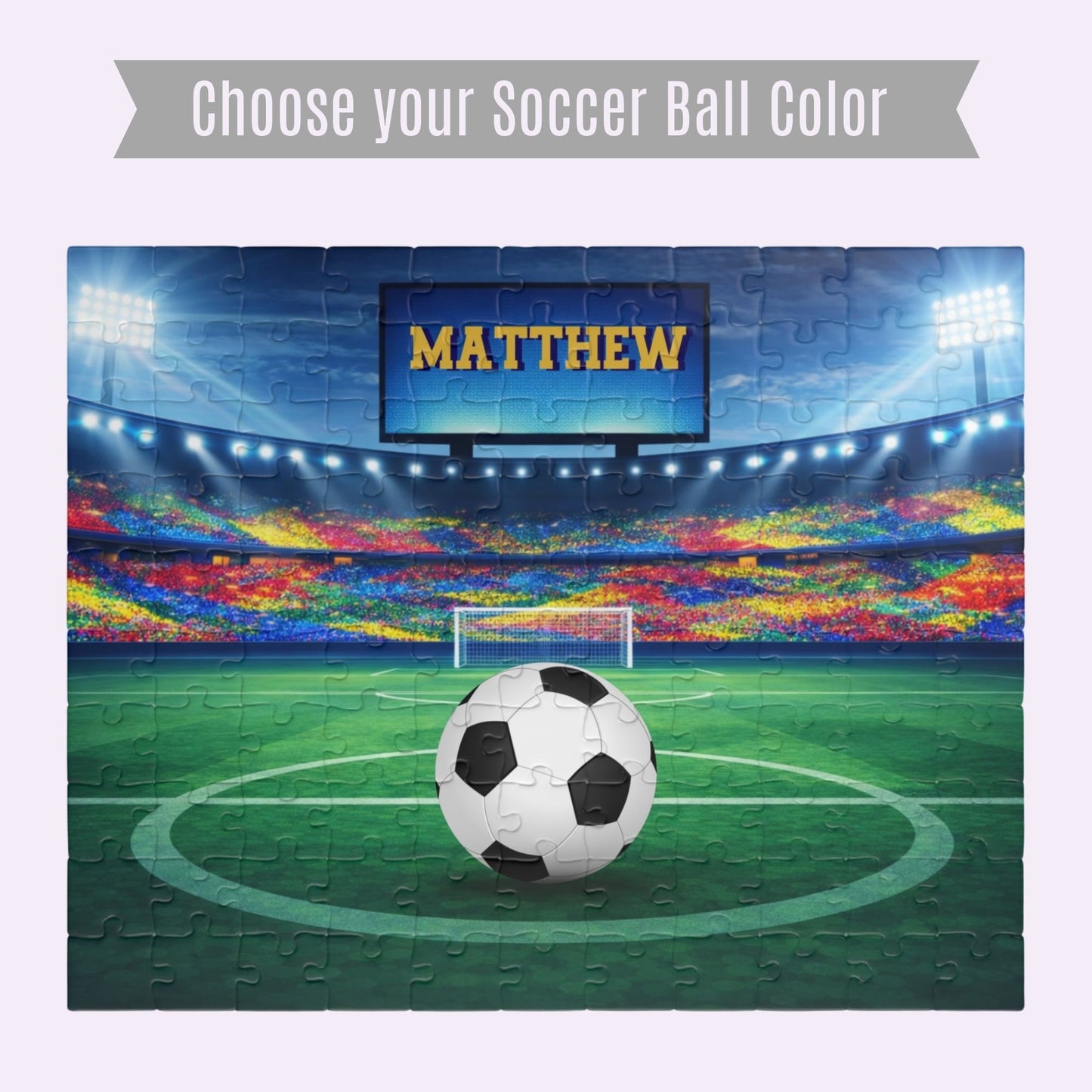 Personalized soccer stadium jigsaw puzzle showing a full stadium scene with a customizable name displayed on the jumbo screen and a customizable soccer ball at center. Image highlights selectable soccer ball color options. 110-piece puzzle.