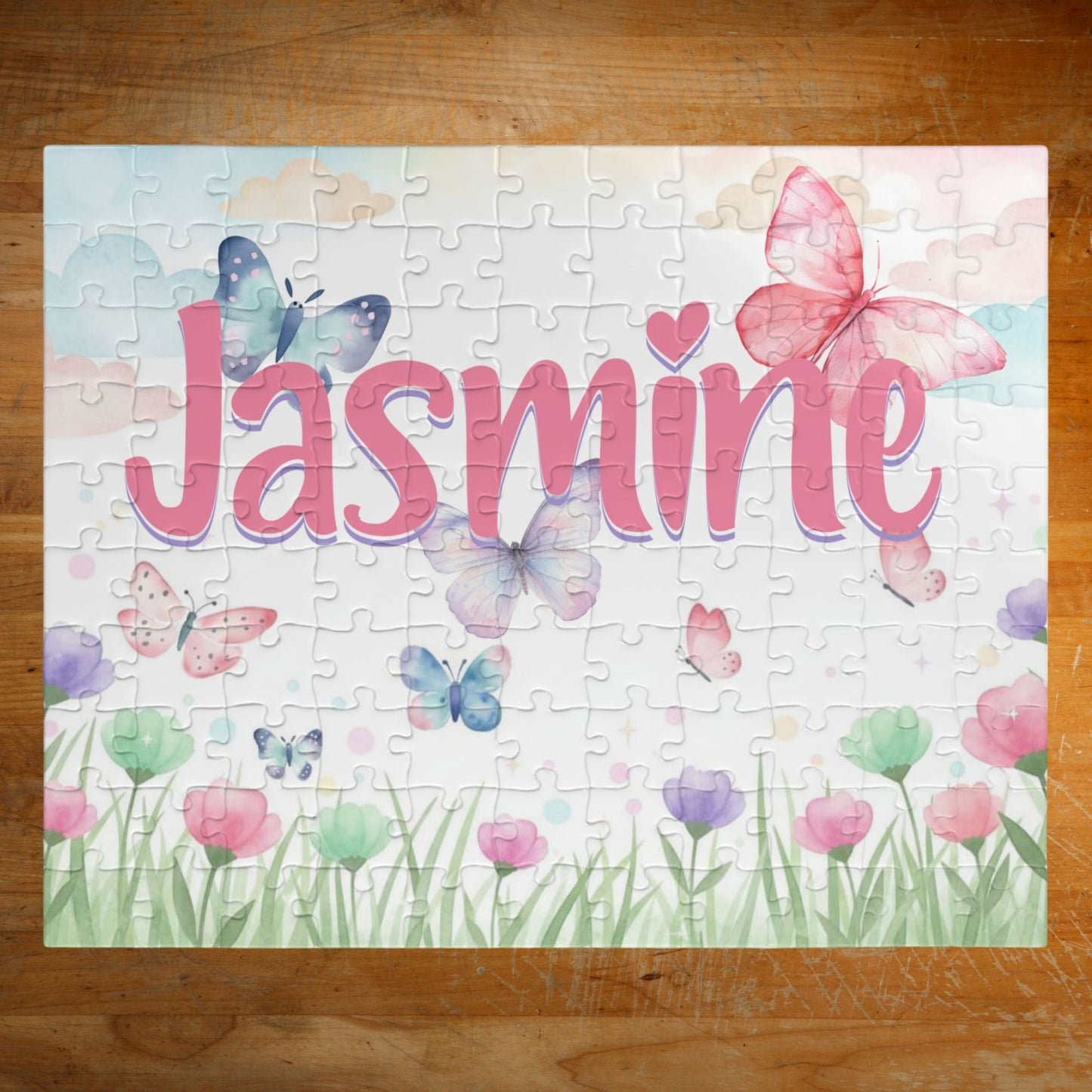 Personalized spring butterfly meadow 110-piece jigsaw puzzle featuring soft pastel flowers, grass, and fluttering butterflies. A customizable name appears prominently across the center of the puzzle design.