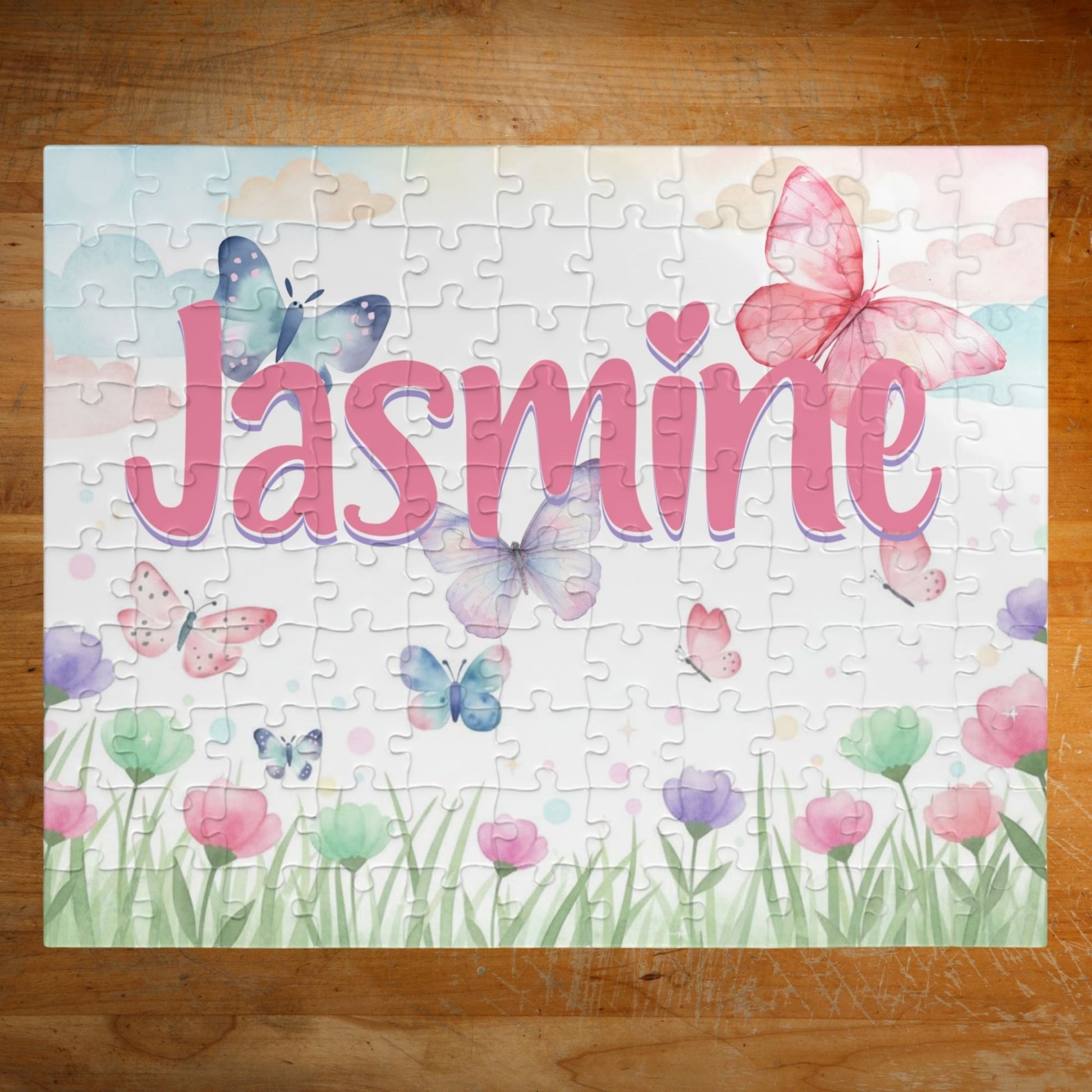 Personalized spring butterfly meadow 110-piece jigsaw puzzle featuring soft pastel flowers, grass, and fluttering butterflies. A customizable name appears prominently across the center of the puzzle design.