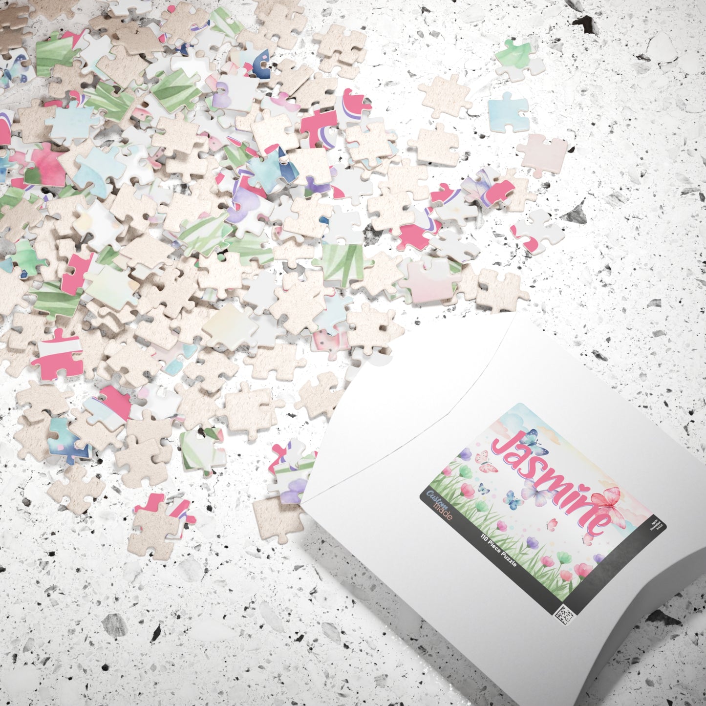 Personalized spring-themed 110-piece jigsaw puzzle displayed with scattered jigsaw pieces and the puzzle box. Features a floral meadow scene with butterflies and a customizable name printed on the puzzle.