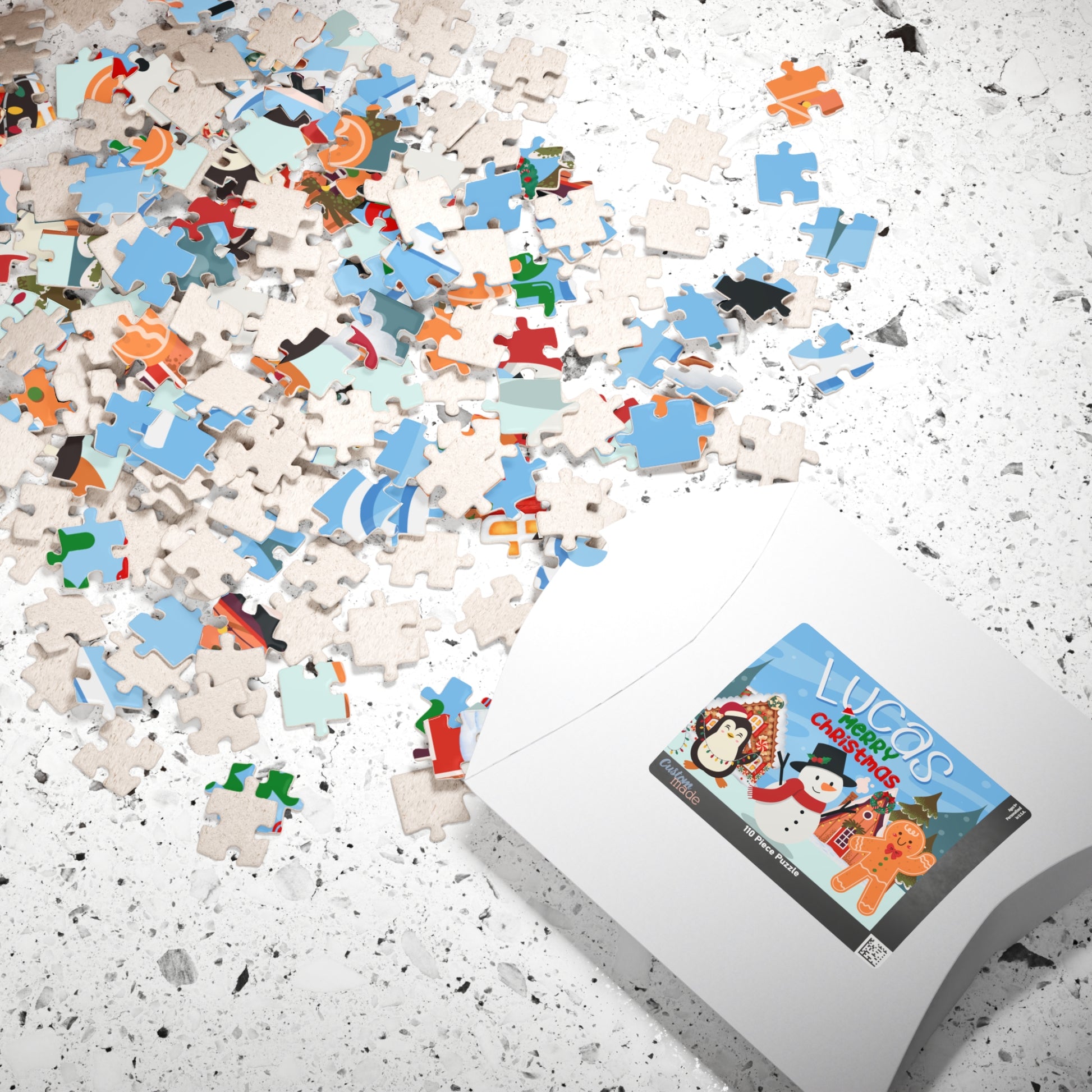 Personalized Christmas puzzle pieces scattered beside the puzzle box featuring a custom name with a snowman, penguin, gingerbread cookie, and festive holiday scene.