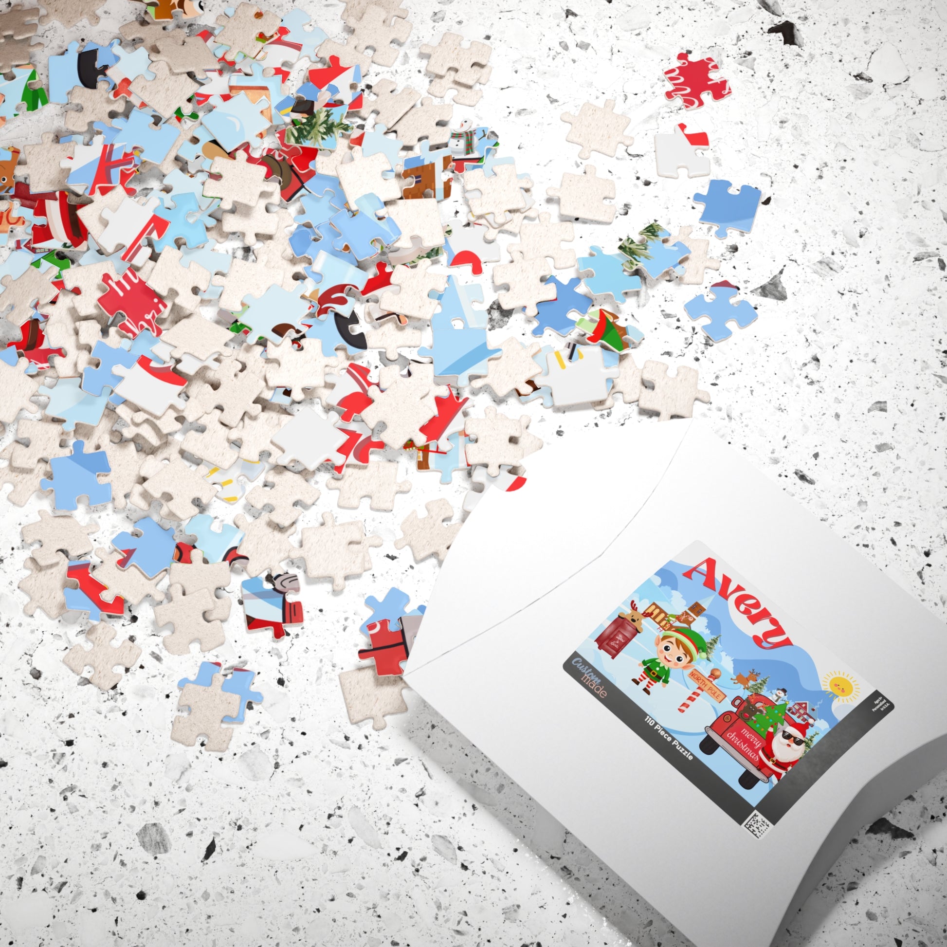 Personalized Christmas puzzle pieces scattered beside the puzzle box, featuring a festive North Pole design with Santa, an elf, reindeer, and a custom child's name.