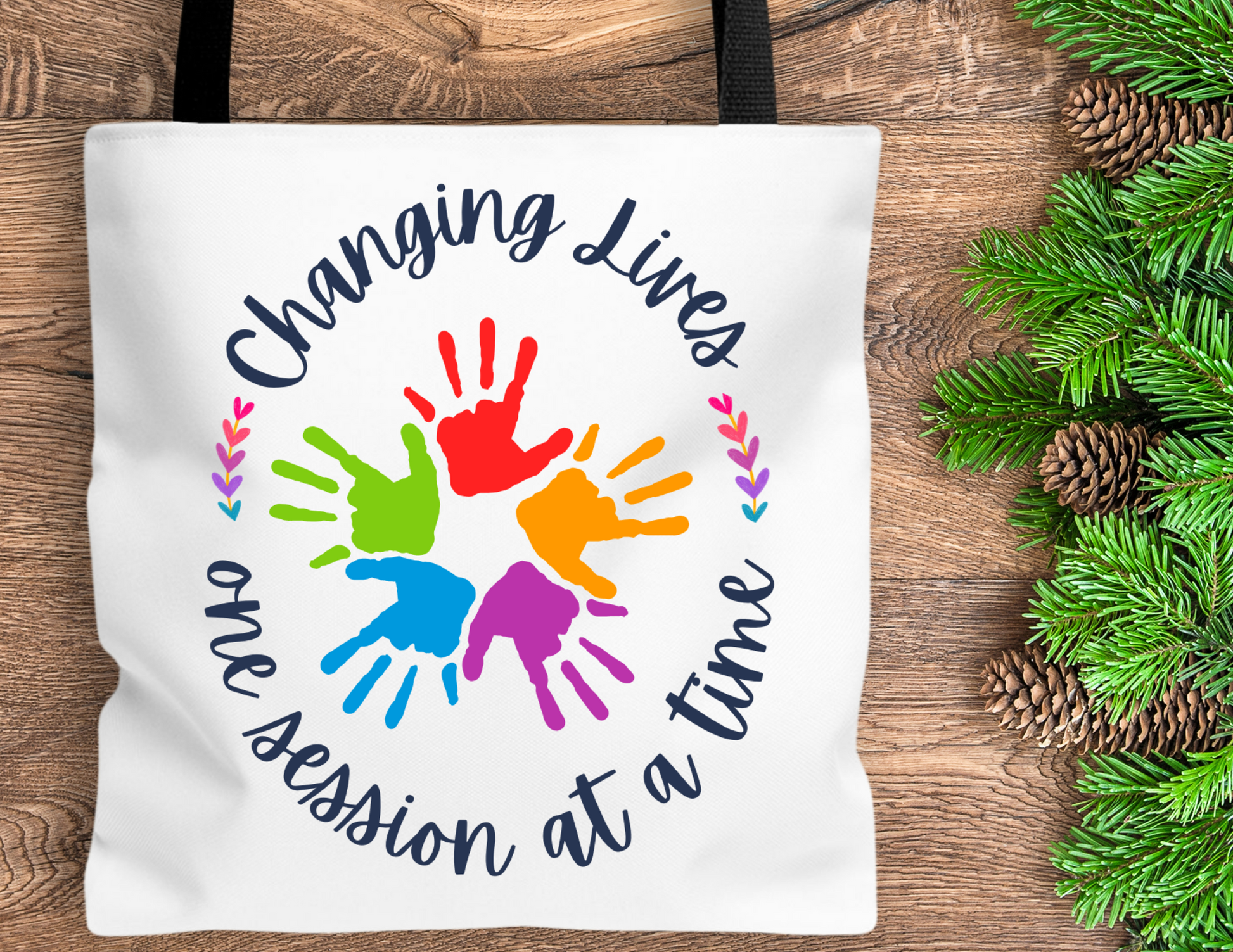 white tote bag that has the quote changing lives one session at a time. In the middle it has different color children&#39;s hands. Perfect for therapist or teacher