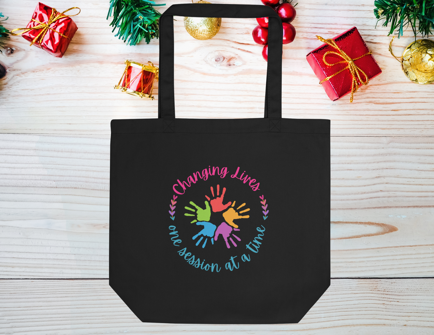 Black Eco tote bag that has the quote changing lives one session at a time. In the middle it has different color children&#39;s hands. Perfect for therapist or teacher