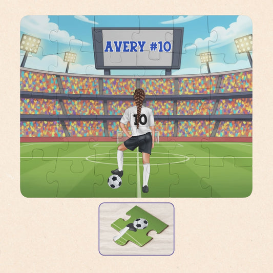 Personalized girls soccer puzzle showing a young player standing on a soccer field inside a large stadium, resting one foot on a soccer ball. The back of the jersey displays a customizable name and number, and a stadium scoreboard above also shows the personalized name and number.