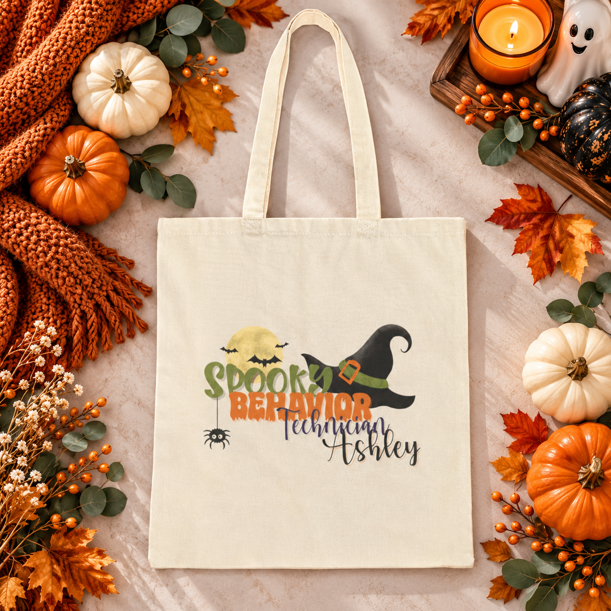 Personalized cotton canvas tote bag in a Halloween-themed lifestyle scene, featuring a spooky design with a witch hat and moon, and a customizable name printed beneath the main design on the front of the bag.