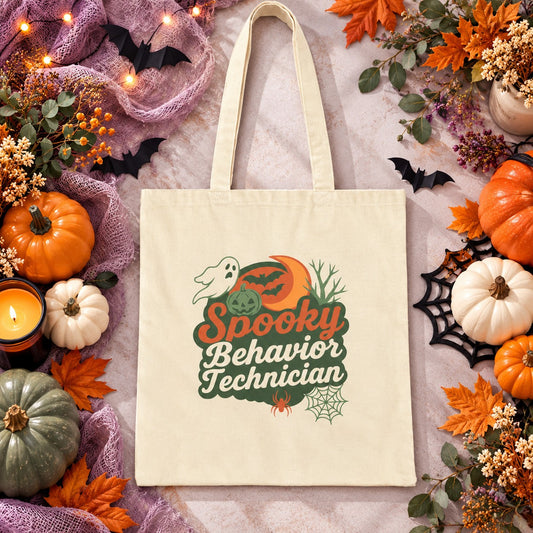 Natural canvas tote bag featuring a Halloween-themed design that reads “Spooky Behavior Technician,” with a ghost, pumpkin, crescent moon, bats, spider, and spiderweb, styled in warm fall colors and displayed against a festive Halloween background.