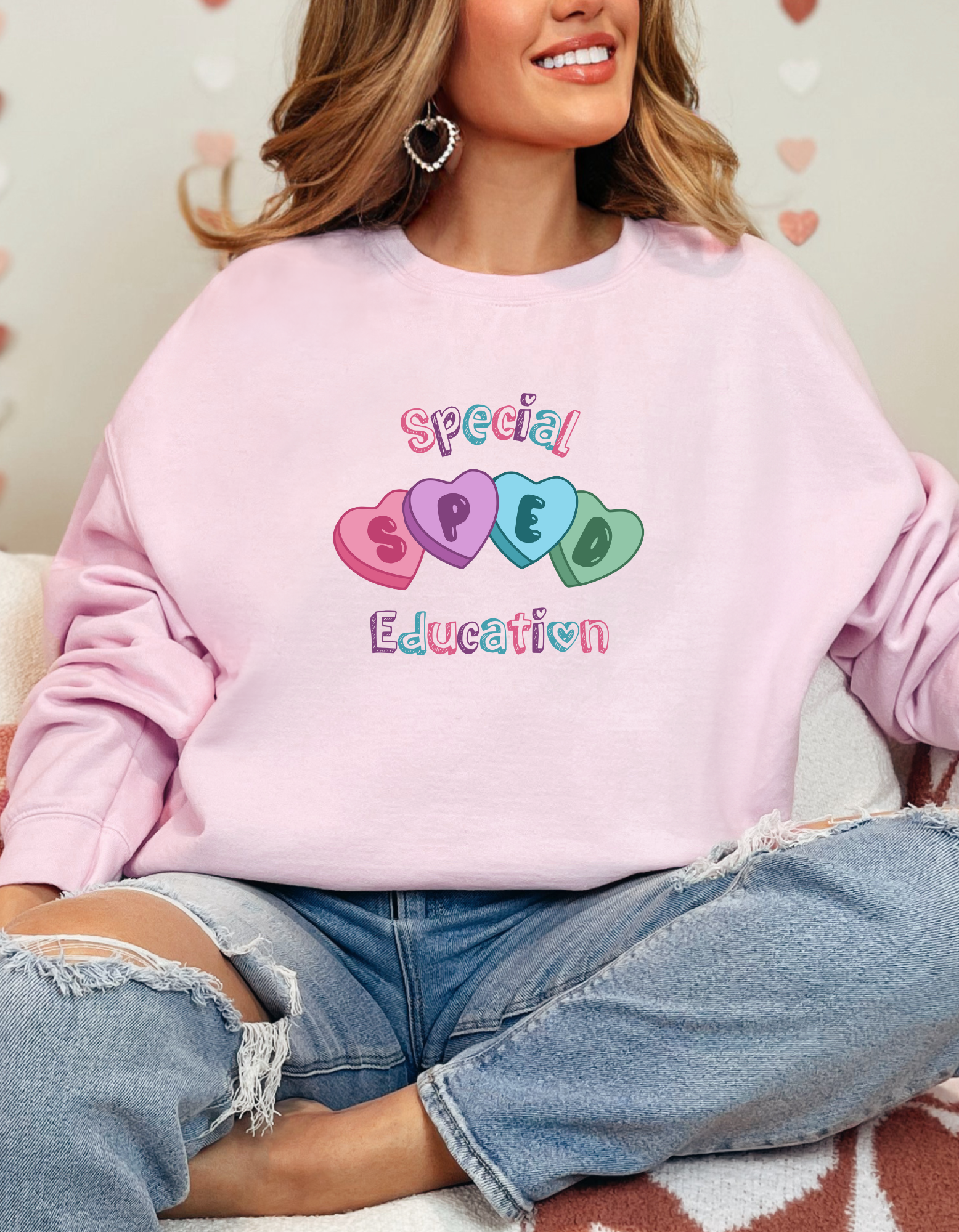 Model wearing a Valentine’s-themed Special Education (SPED) crewneck sweatshirt featuring colorful heart graphics and playful lettering across the chest, shown in a light pink option and available in a variety of colors for a cozy, casual fit.