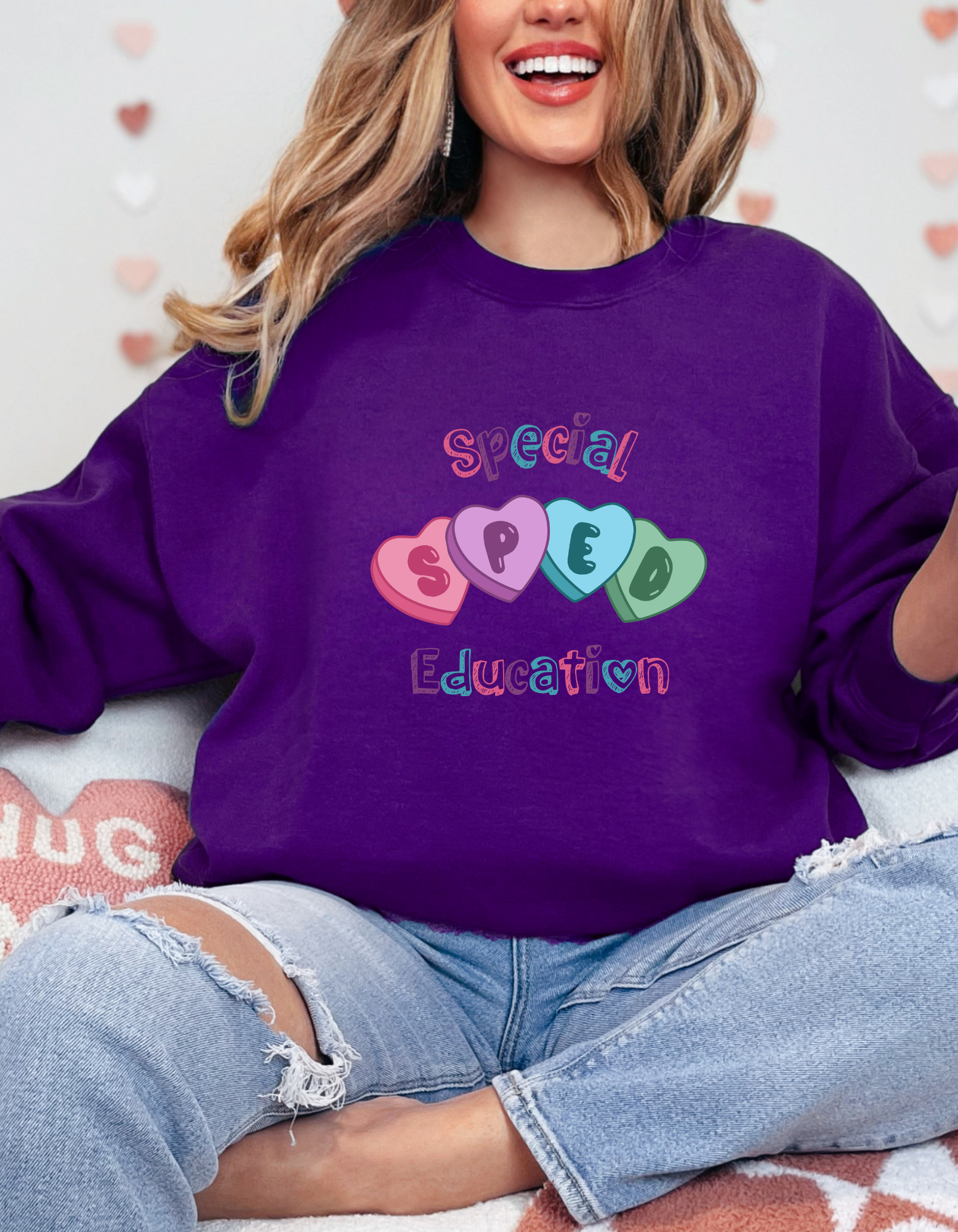 Model wearing a Valentine’s-themed Special Education (SPED) crewneck sweatshirt featuring colorful heart graphics and playful lettering across the chest, shown in a light pink option and available in a variety of colors for a cozy, casual fit.